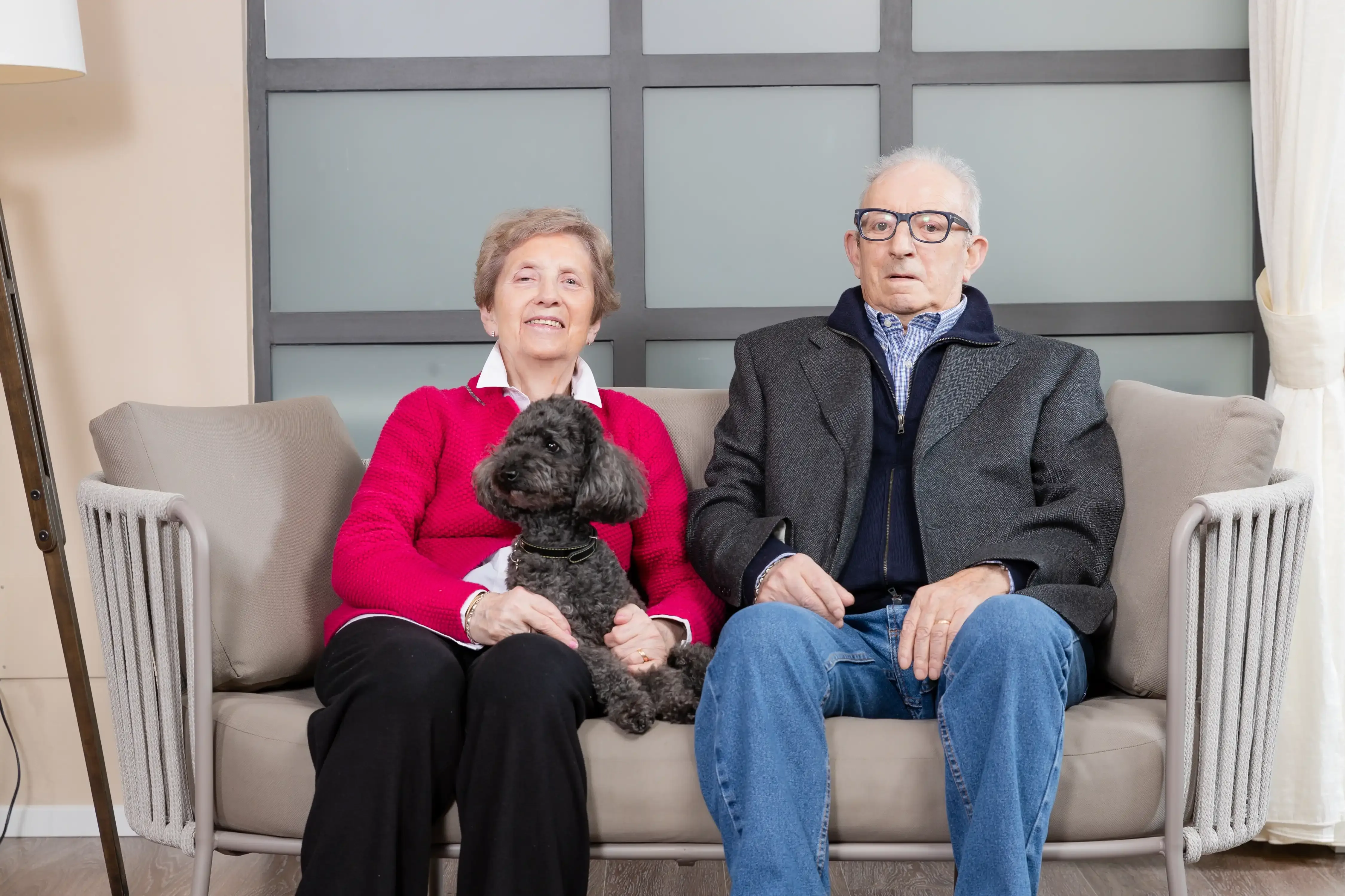 Coppia di anziani seduti su un divano con un cane nero in grembo