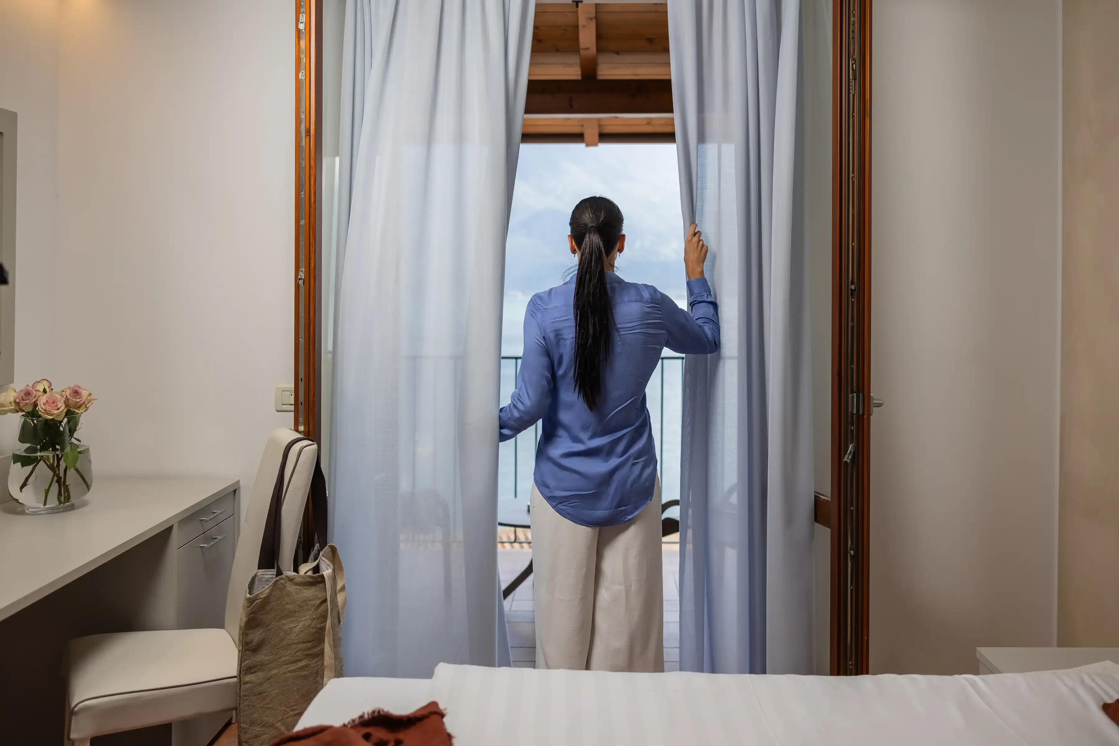 Donna apre le tende in una stanza con vista sul mare
