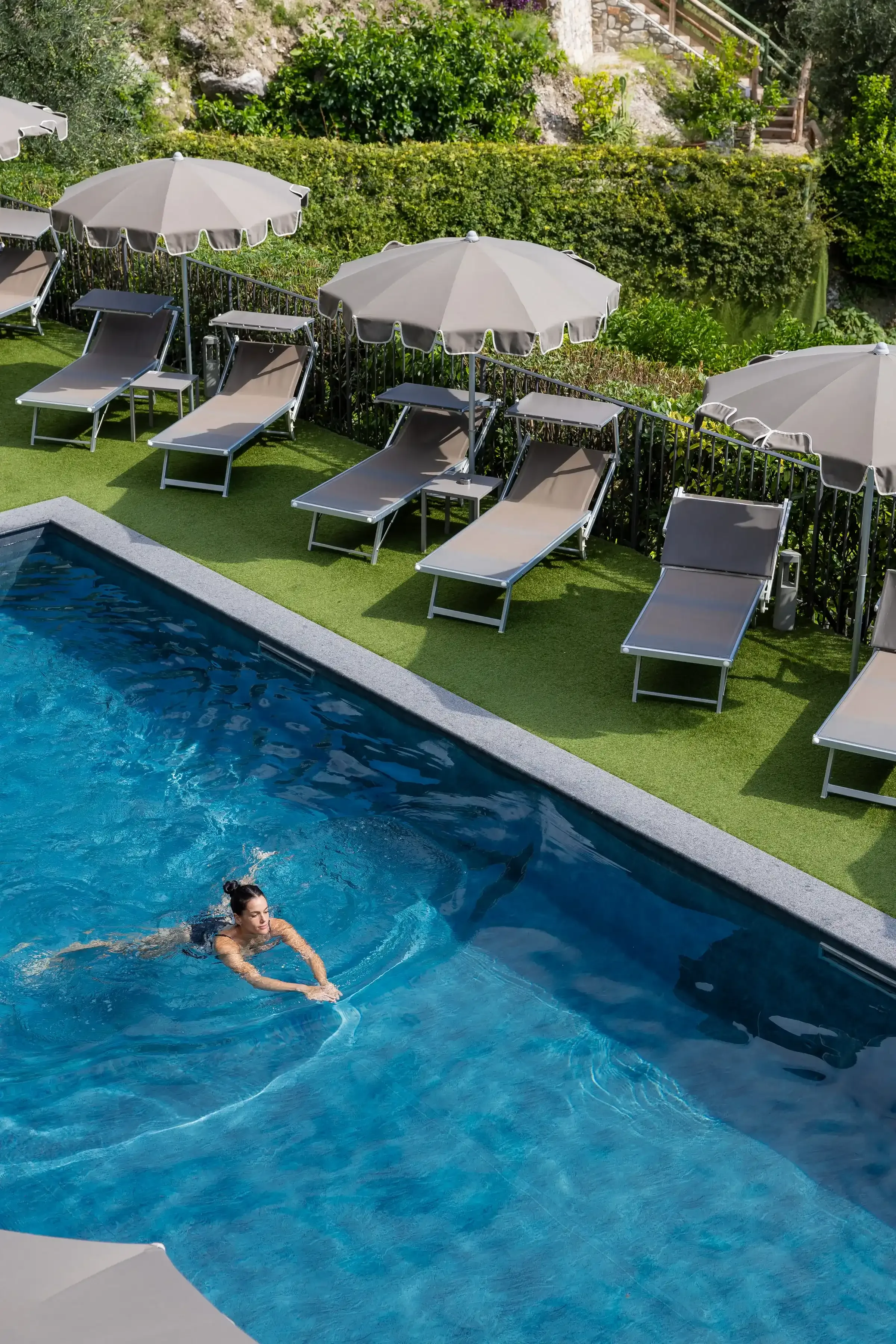 Femme nageant dans une piscine extérieure avec transats et parasols