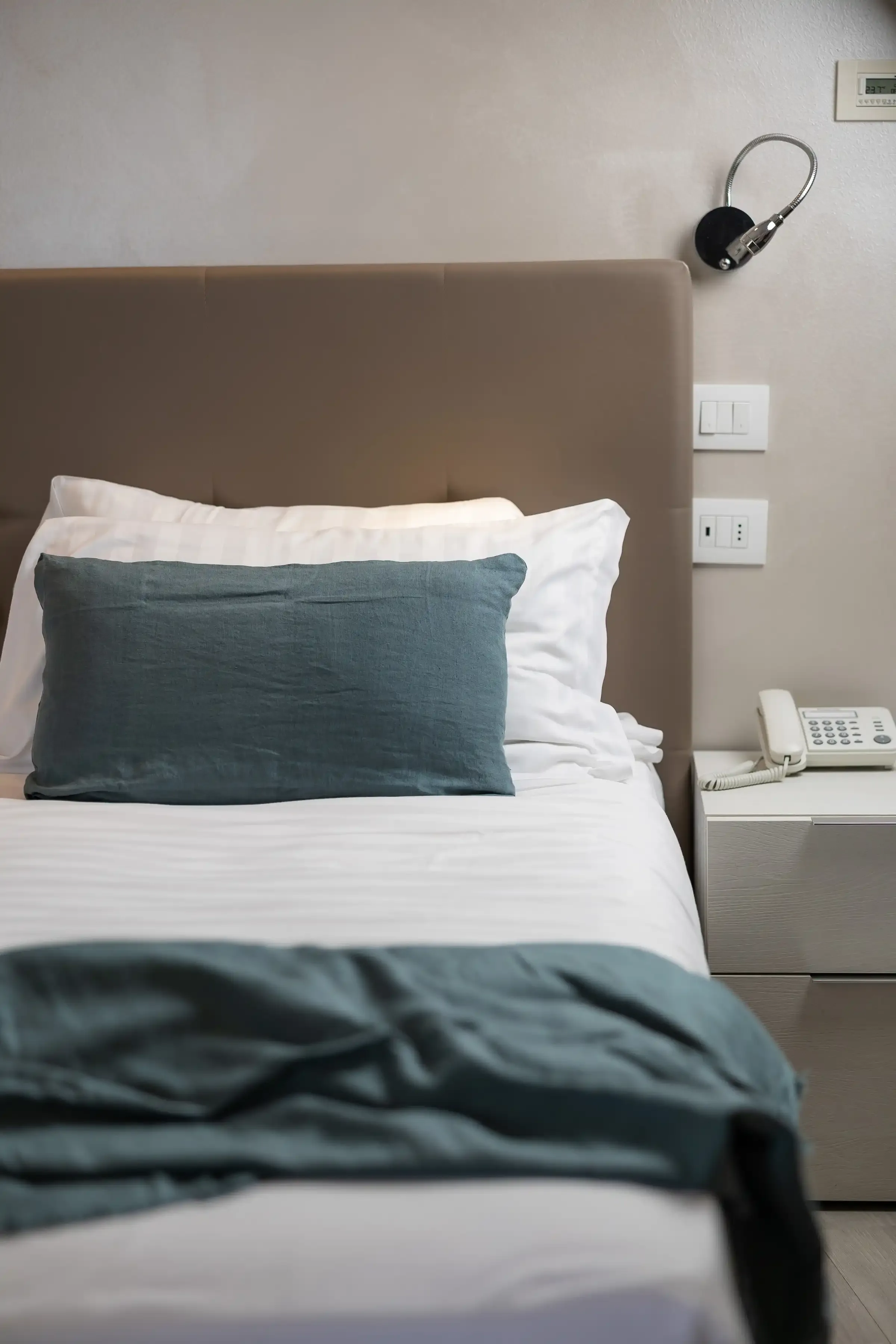 Letto singolo con cuscino verde e comodino bianco in camera d'albergo