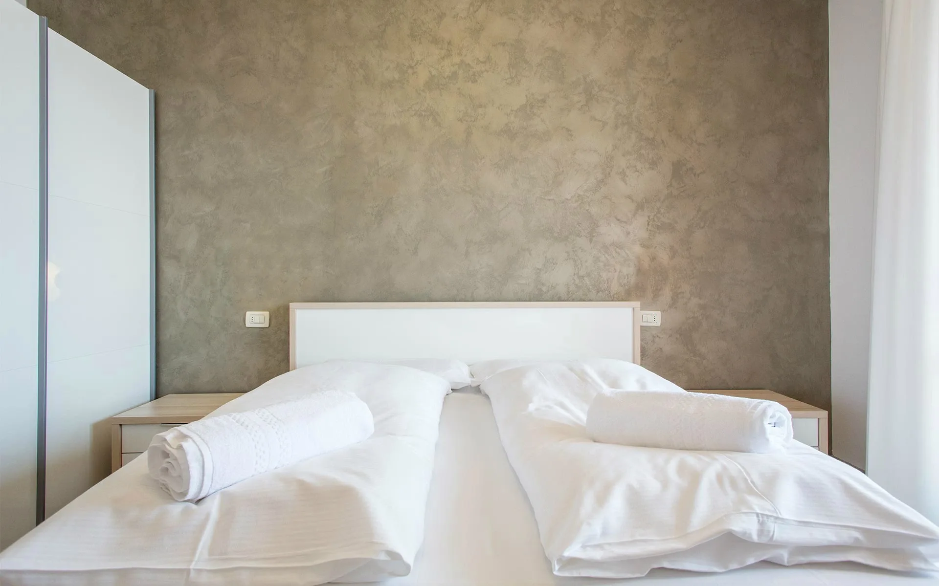 Lit double moderne avec draps blancs et serviettes roulées