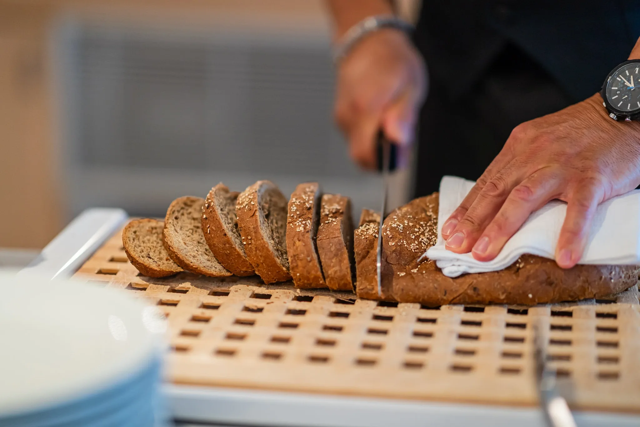 Mani che affettano pane integrale su un tagliere