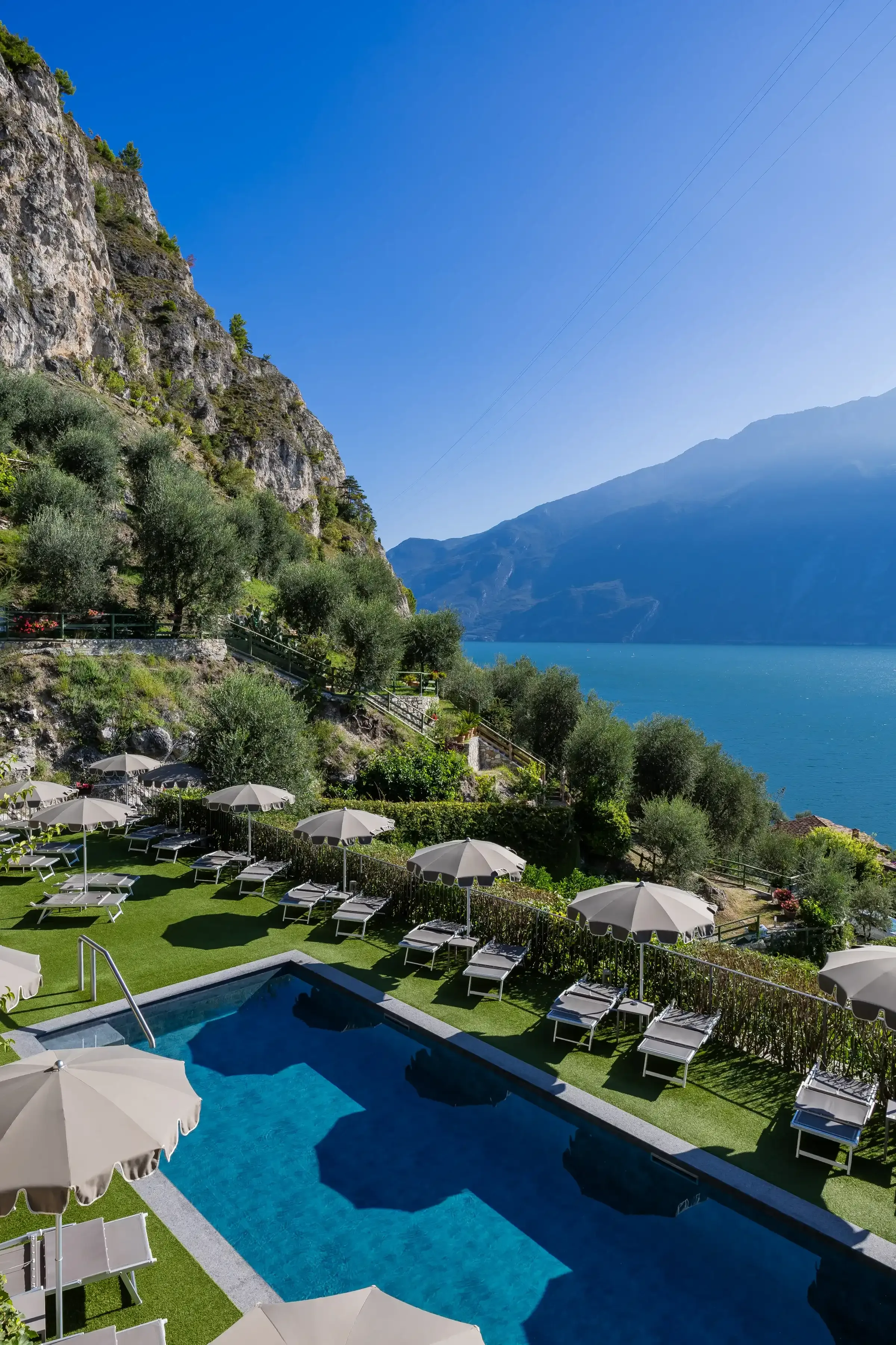 Piscina con lettini e ombrelloni vista Lago di Garda e montagne