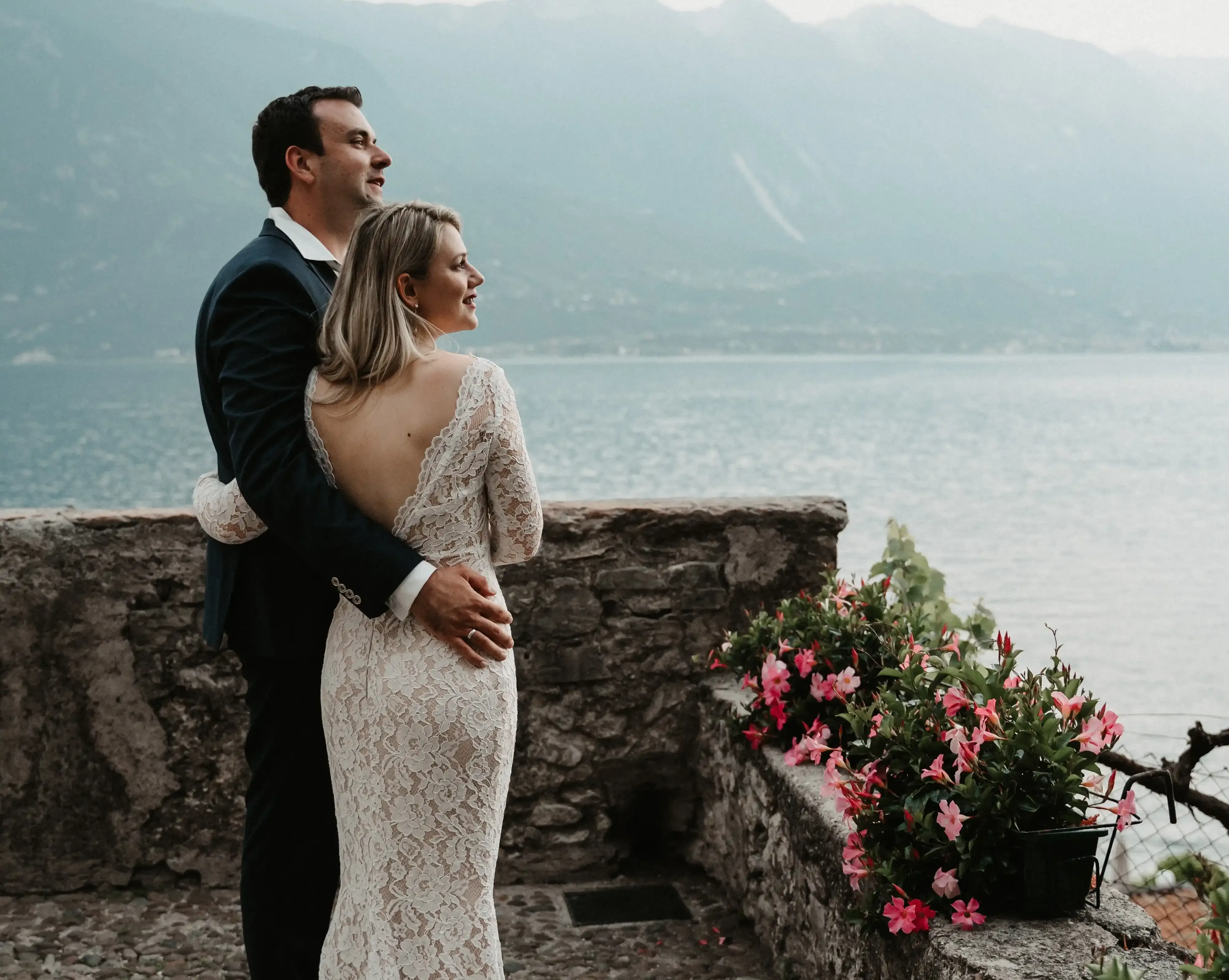Coppia di sposi abbracciati con vista lago e fiori