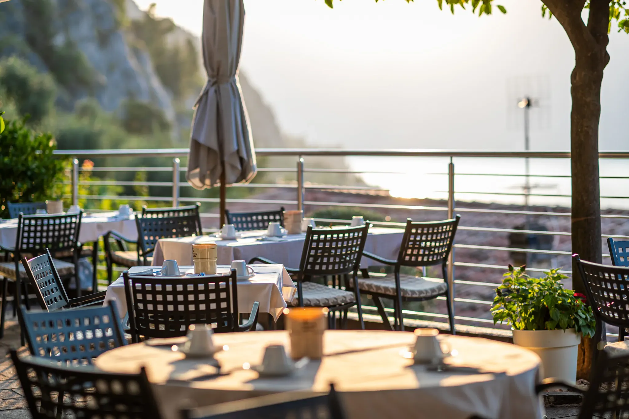 Terrazza di un ristorante con tavoli apparecchiati e vista sul mare al tramonto