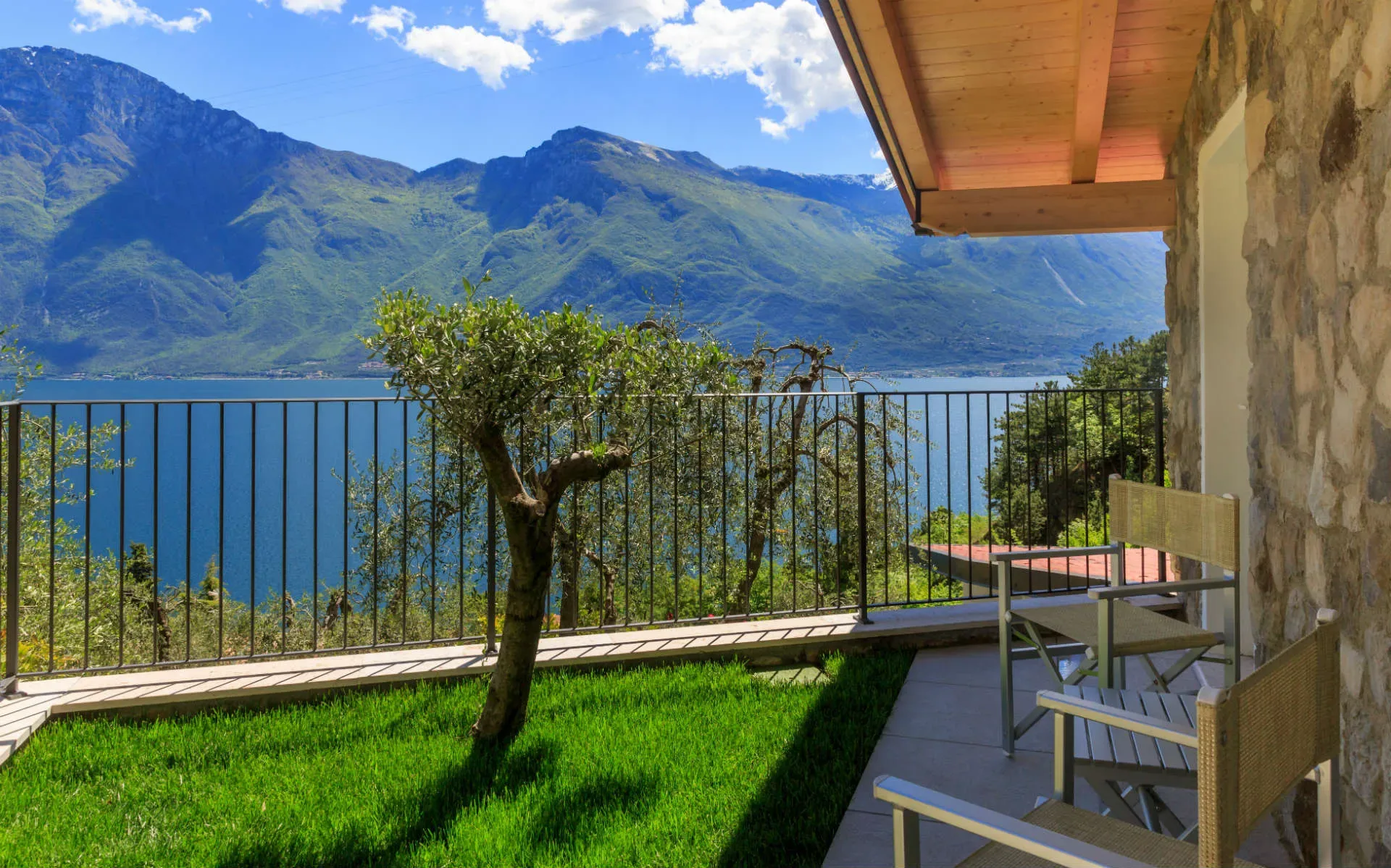 Vista sul lago e sulle montagne da una terrazza con sedie e giardino